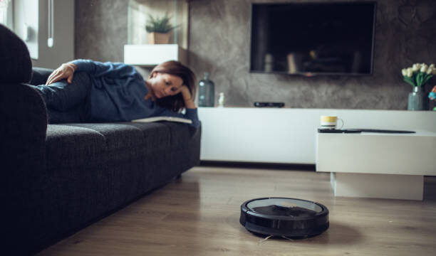 Robotic Vacuum Cleaner Cleaning Floor While Woman reading book
